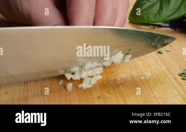 chef-chops-fresh-garlic-cloves-on-a-wooden-cutting-board-with-a-metal