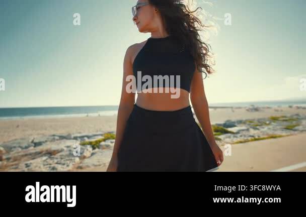 a-woman-walks-along-the-beach-wearing-sunglasses-and-sportswear-the
