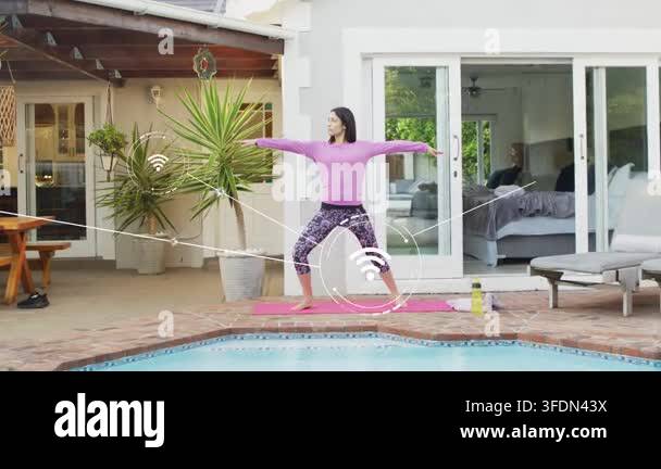 Woman stepping onto pink mat and holding Warrior II beside pool, wifi ...