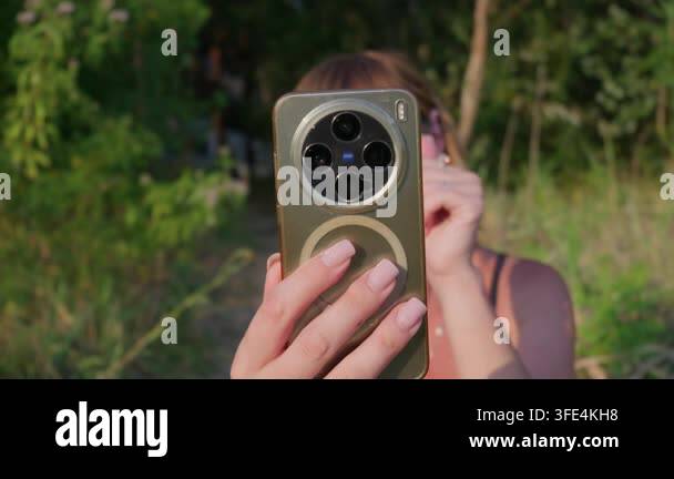 Photo Sensor Array A woman holds a modern gold smartphone covering her face in a lush ...