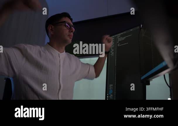 A man wearing glasses working late at night, looking at code on a ...