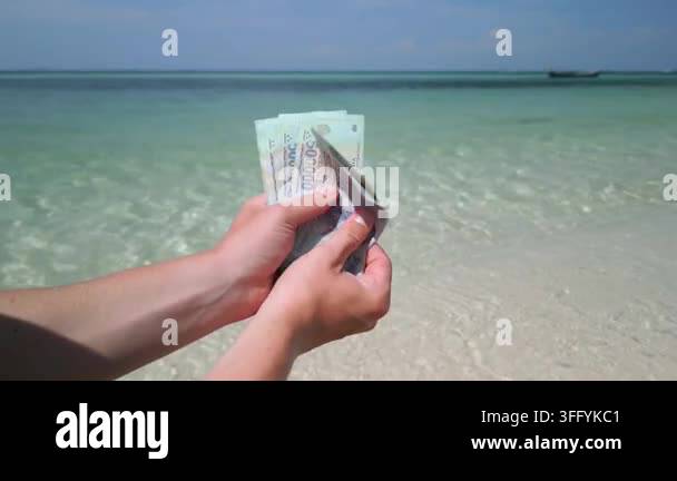 Close-up of hands holding Vietnamese dong banknotes on a tropical beach ...