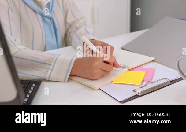 Person writing in a notebook with colorful sticky notes on a white desk ...