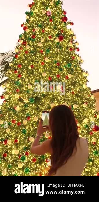 A woman photographs a giant Christmas tree covered in colorful ...