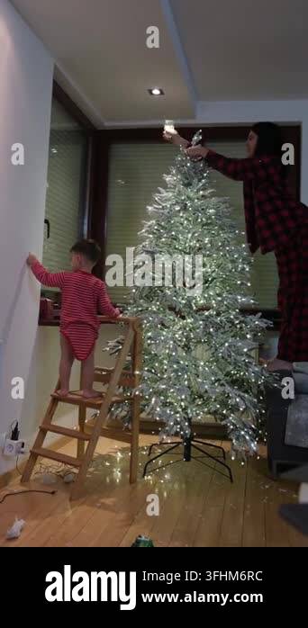Family decorates a glowing Christmas tree in a cozy home living room ...