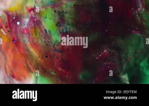 Macro view of swirling red and green liquids mixed with iridescent ...