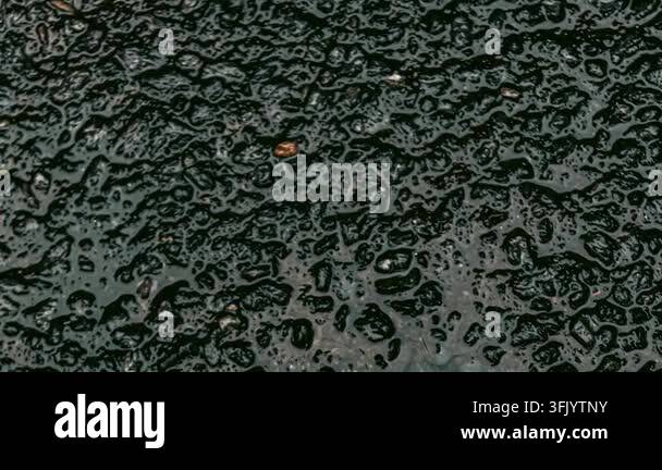 Close-up abstract view of wet dark asphalt pavement showing textured ...