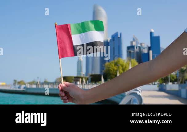 Female hand holding small UAE flag against Abu Dhabi skyline. Symbol of ...
