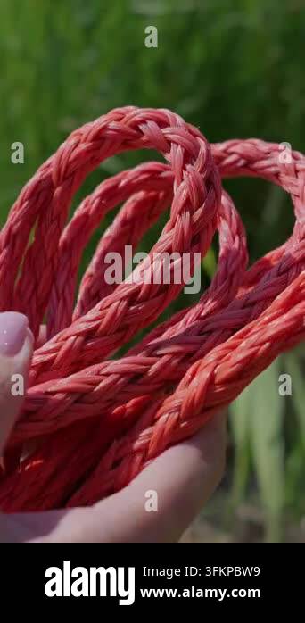Hand Twisted Rope Braided red synthetic cord is held by a hand in an outdoor setting. The ...