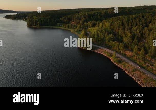 Aerial view of a winding road alongside a dark blue lake and lush green ...