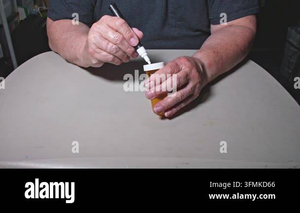 A person uses a marker to write on a container while sitting at a table ...
