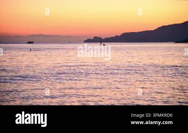 Silhouette of paddleboarder and fishing boat on calm sea at sunset ...