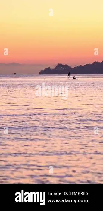 Silhouette of paddleboarder and fishing boat on calm sea at sunset ...