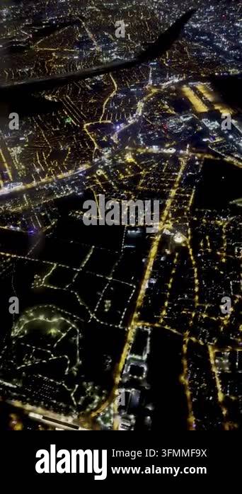 Night aerial view of glowing city lights and airplane wing from above ...