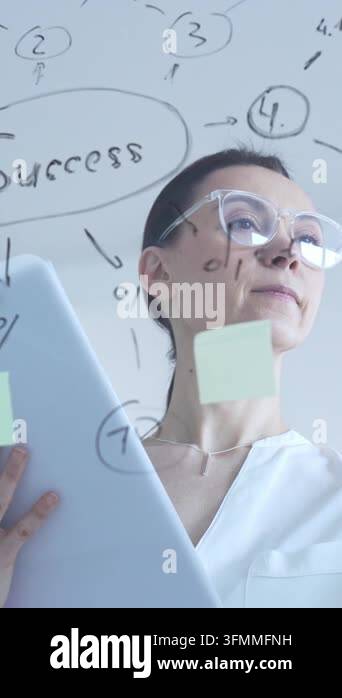 Businesswoman standing in front of a glass board, actively engaging ...
