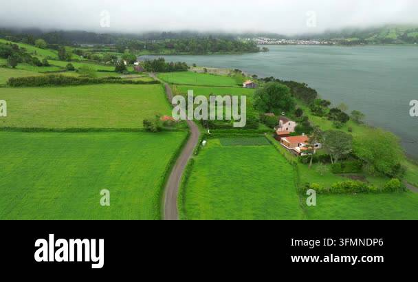 Aerial view of a winding road through lush green fields and a lakeside ...
