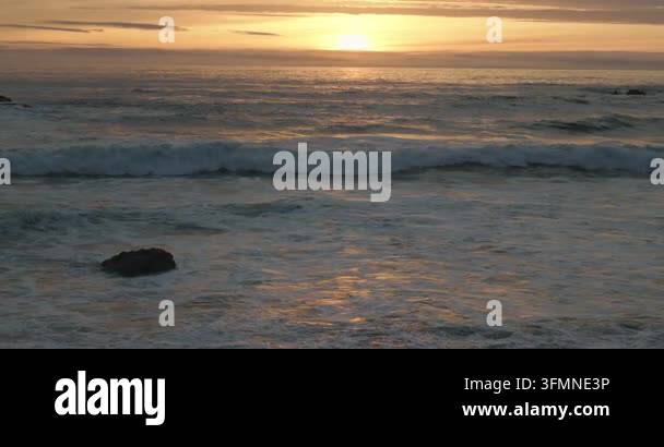 Sunset over ocean waves with golden reflections near rocky shoreline ...