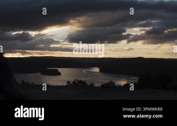 Dramatic sunset over a calm lake with dark, moody clouds and sun rays ...
