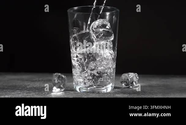 Water pouring into glass with ice cubes and splashing in super slow ...