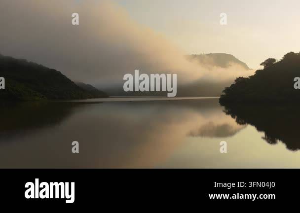 Misty mountains overlooking calm lake reflecting soft dawn light Stock ...
