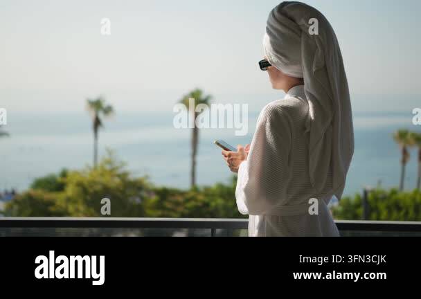 Young woman in a hotel robe types a message on her smartphone while ...