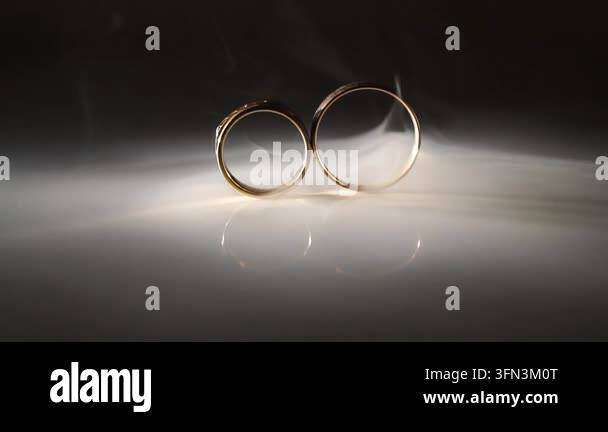 Gold wedding rings are elegantly displayed on a reflective surface ...