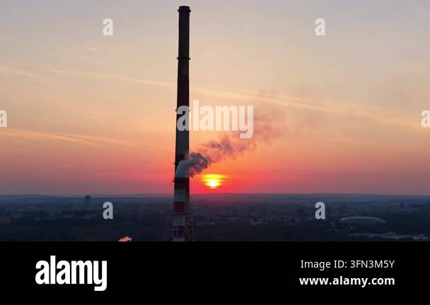 Industrial smokestack emits steam against a vibrant sunset backdrop ...