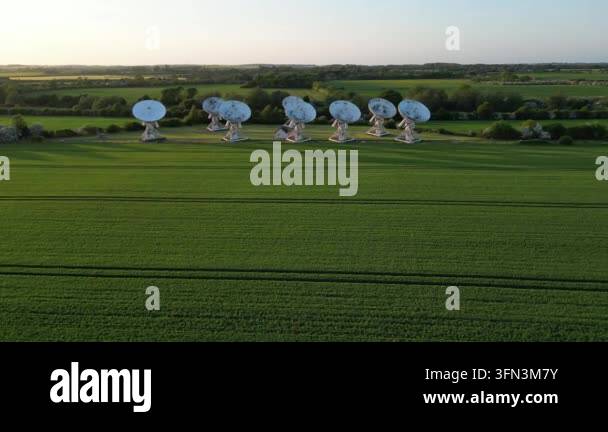 Aerial drone footage of a radio telescope array in a green field at ...