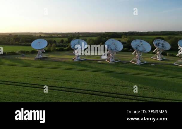 Aerial drone footage of a radio telescope array in a green field at ...