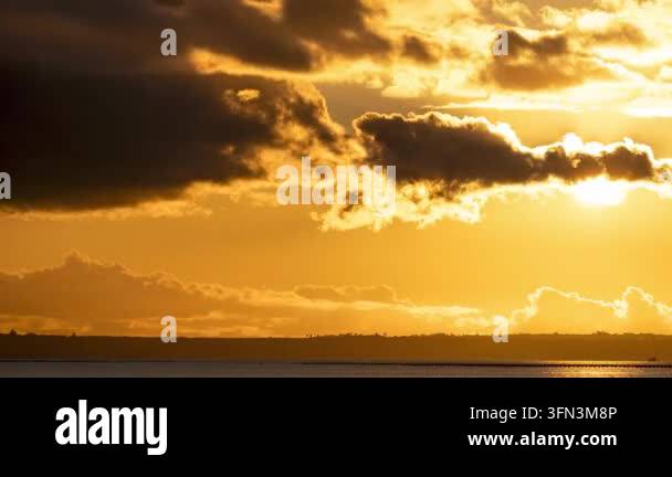 Golden sunset sky with dramatic clouds moving over the ocean horizon ...