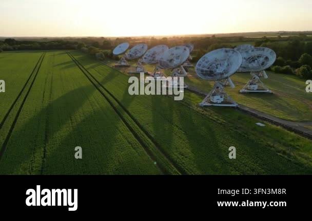 Aerial drone footage of a radio telescope array in a green field during ...