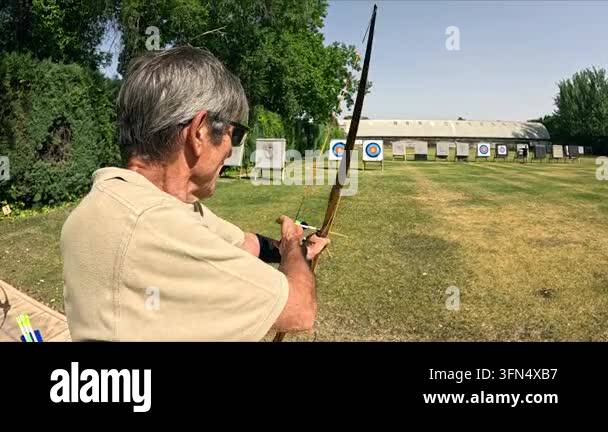 Concentrated senior archer practicing at an outdoor range. He nocks an ...