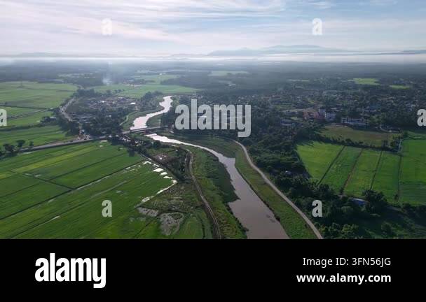 Aerial view of a winding river through lush green fields at Perai ...