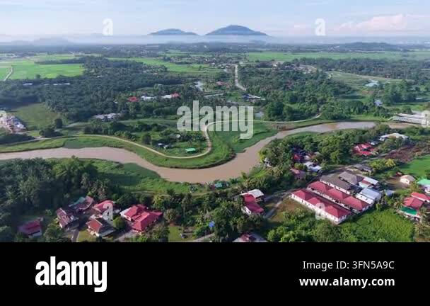 Aerial view of a river winding through a lush village. Red roofed homes ...