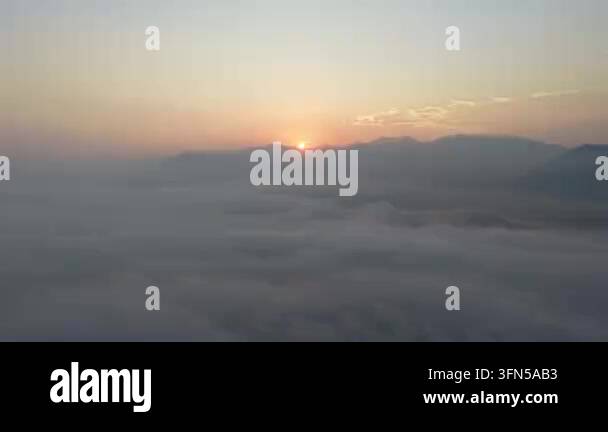 Sunrise peeks over a mist covered mountain range with soft clouds ...