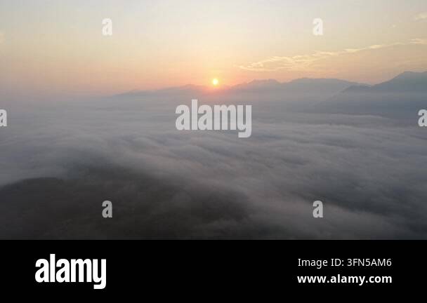 Beautiful sunrise over mist covered mountains with soft clouds and calm ...