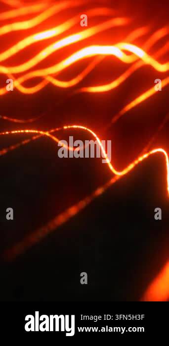 Abstract orange and yellow neon waveforms glowing against a dark ...