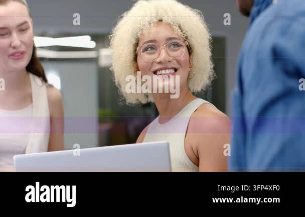 Seated woman typing at laptop, activating waveform while team leaning ...