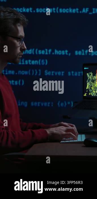 Side view, coder at a dark office desk works late at night, with ...