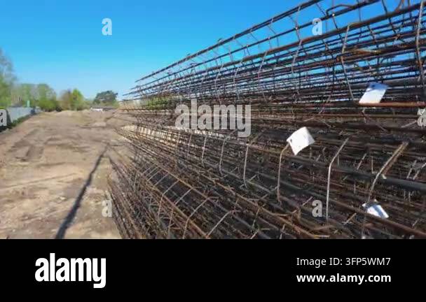 A large stack of rusty cylindrical metal rebar cages sits on a ...