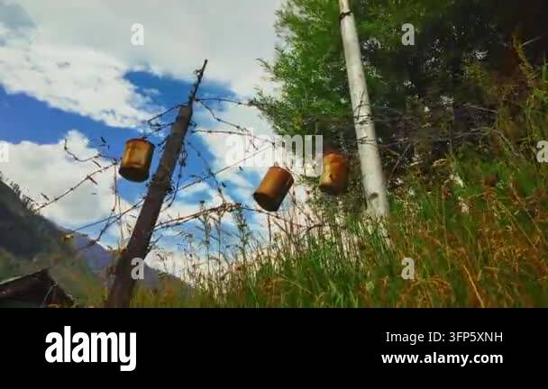 Rusty cans hang from a barbed wire fence against a cloudy blue sky and ...