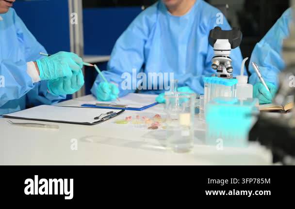 Scientists in blue lab coats and gloves working at a table with ...
