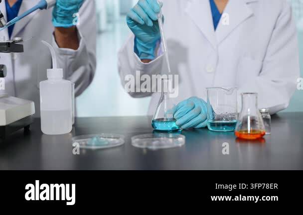 Two scientists in lab coats and blue gloves are conducting an ...
