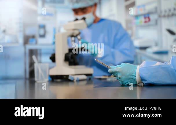 Two scientists in a laboratory, one using a microscope and the other ...