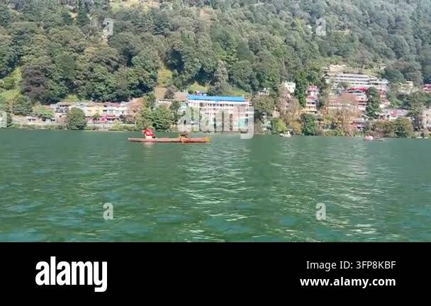 Two people are rowing a small boat on a calm lake with a tree-covered ...