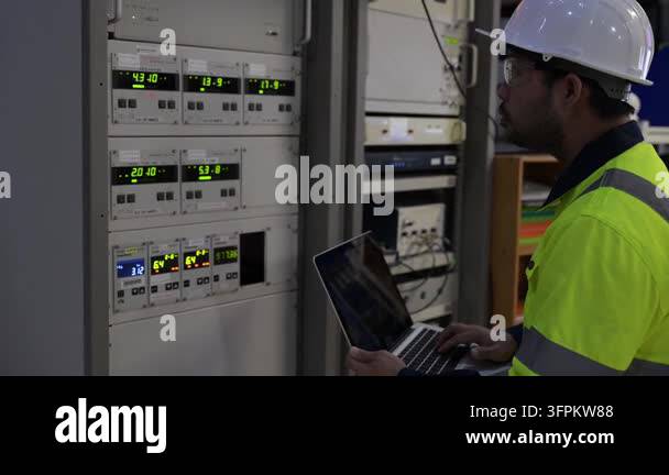 Engineer in a hard hat and high-visibility vest types on a laptop next ...