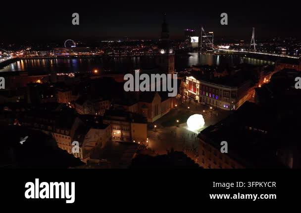 Night aerial over Riga old town to St Peters tower with lit bridges and ...