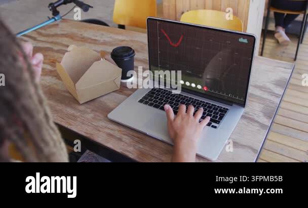 Male typing, handling takeout pastry while red plot animating on laptop ...