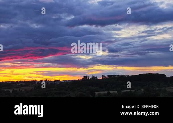 Golden and gray clouds drift across a blue evening sky above a dry ...