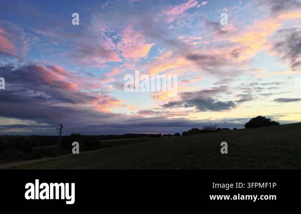 Golden and gray clouds drift across a blue evening sky above a dry ...